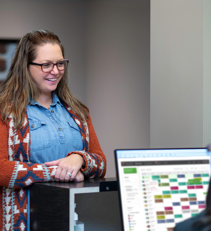 McKnight Signature Dental Smiling patient in a denim shirt and sweater standing at the reception desk while scheduling an appointment.