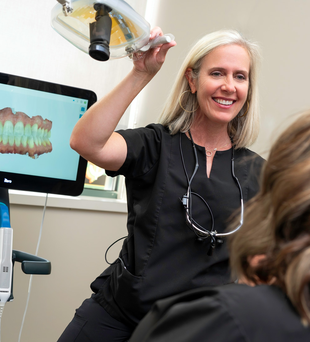 McKnight Signature Dental Dental professional in black scrubs adjusting an overhead light in a treatment room, with a digital dental scan displayed on a monitor.